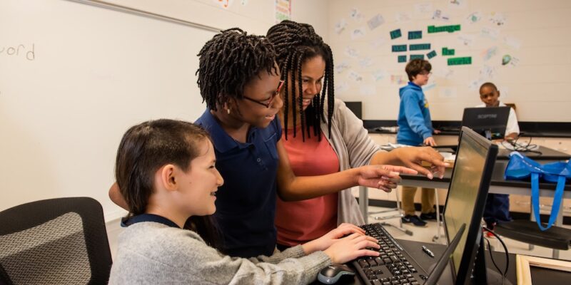 An educator helps students with a coding task.
