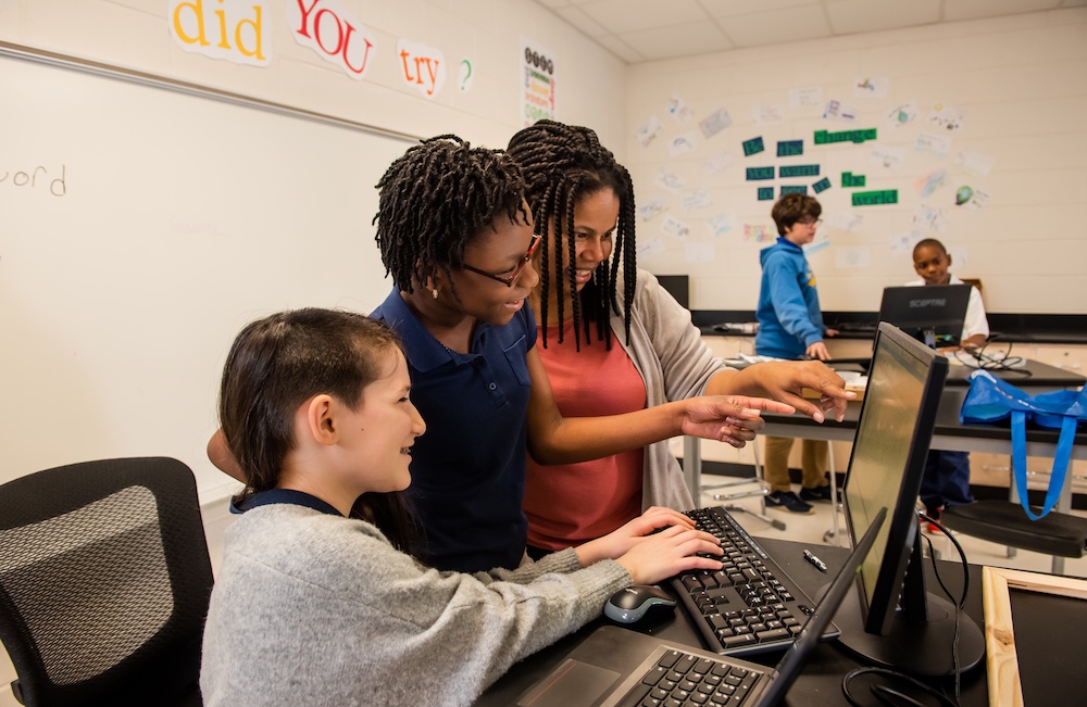 An educator helps students with a coding task.