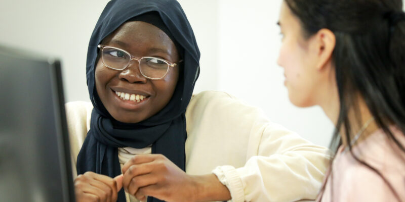 Two students are seated at a desk, collaborating on a computing task.