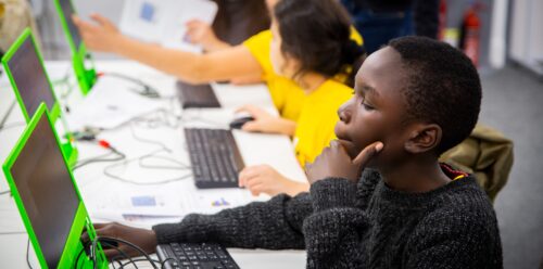 Photo of young people sitting at a desk, working on small computers.