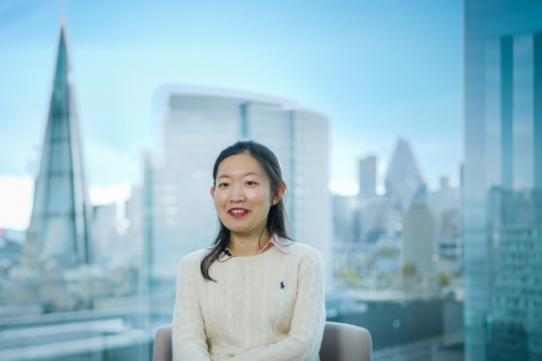 A woman is pictured sitting in the office. There's a window behind her with a view of the London skyline.